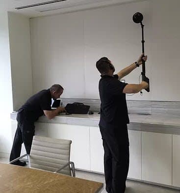 Two technicians sweeping a conference room with a ceiling-height antenna mast